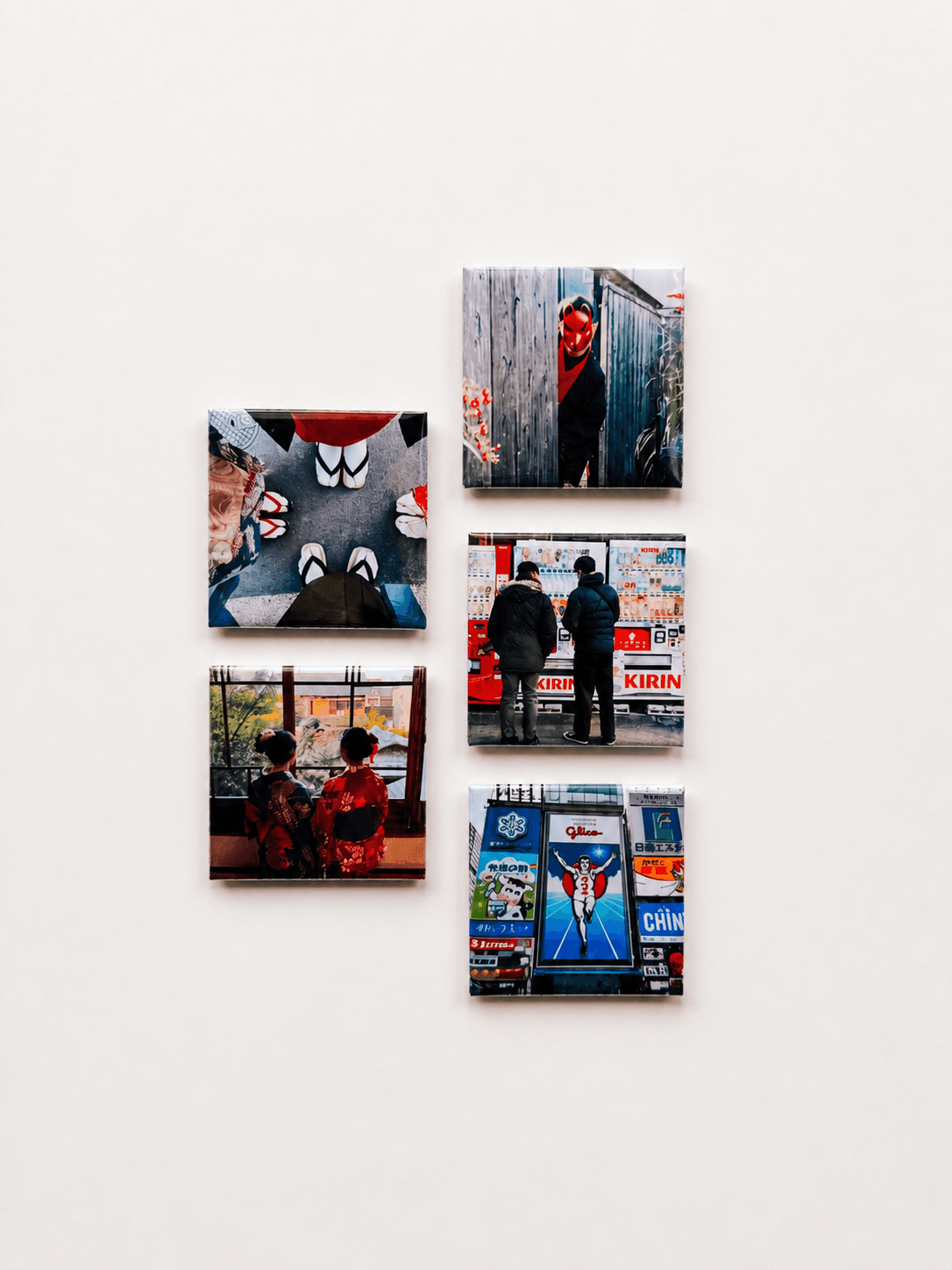 Five square photo magnets of Japan travel scenes, arranged loosely on a pale surface